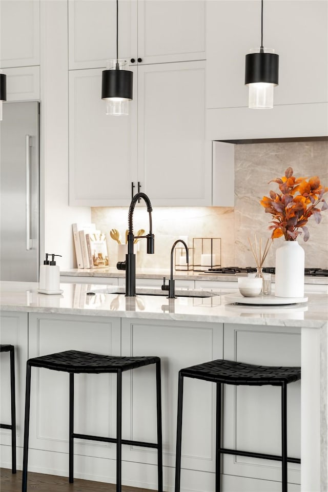 kitchen with pendant lighting, high end refrigerator, light stone countertops, and white cabinets