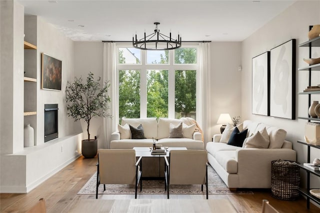 living area with a glass covered fireplace, a notable chandelier, baseboards, and wood finished floors