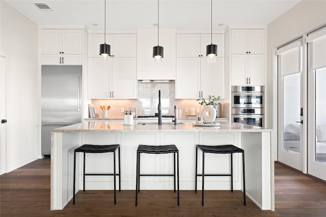 kitchen featuring hanging light fixtures, appliances with stainless steel finishes, a kitchen island with sink, and white cabinets