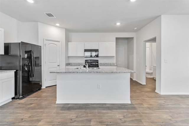 kitchen featuring light stone counters, a center island with sink, and black appliances