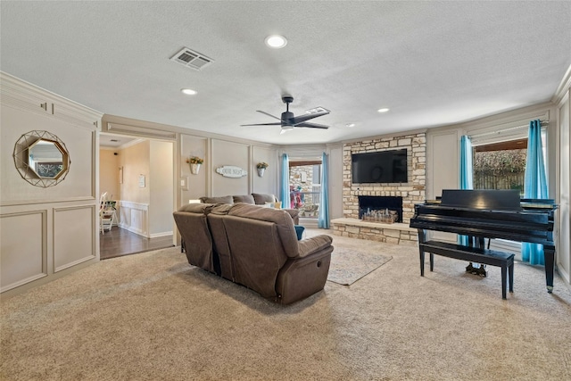 living room with a fireplace, a textured ceiling, ceiling fan, carpet, and ornamental molding