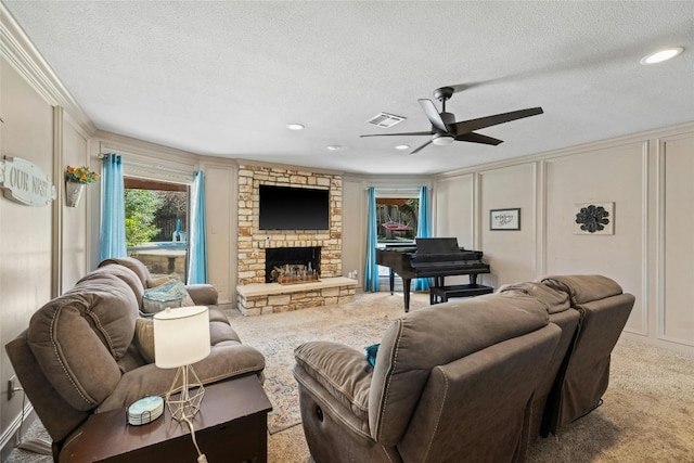 carpeted living room featuring ceiling fan, a stone fireplace, a textured ceiling, and ornamental molding