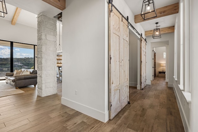 hall featuring beam ceiling, decorative columns, hardwood / wood-style floors, and a barn door