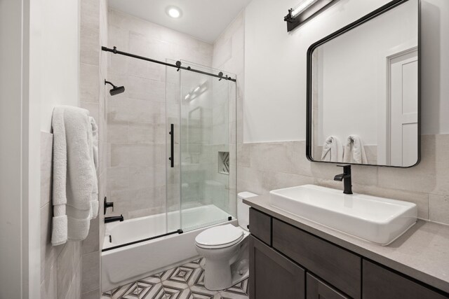 full bathroom featuring enclosed tub / shower combo, tile walls, vanity, and toilet