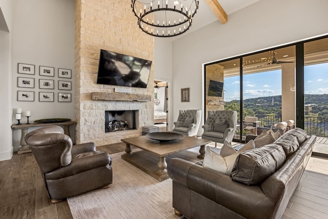 living room featuring a stone fireplace, a high ceiling, beam ceiling, hardwood / wood-style flooring, and a notable chandelier