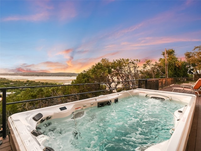 pool at dusk with a hot tub and a water view