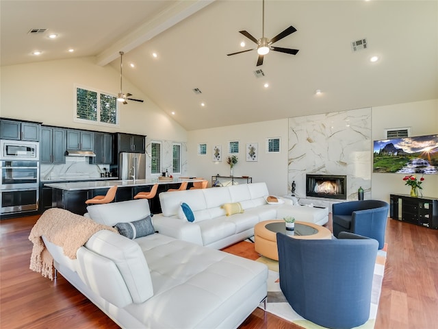 living room with wood-type flooring, a high end fireplace, beamed ceiling, high vaulted ceiling, and ceiling fan