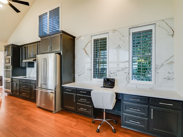 office area featuring light wood-type flooring, built in desk, ceiling fan, and vaulted ceiling