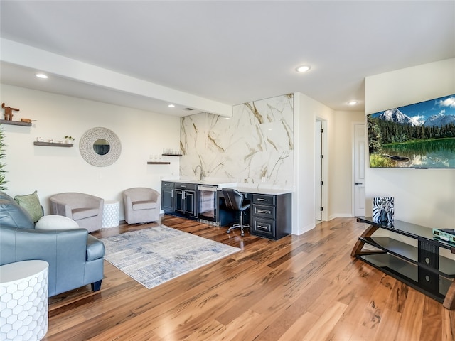 living room featuring bar, beam ceiling, beverage cooler, built in desk, and light hardwood / wood-style floors