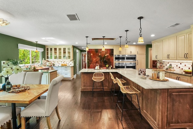 kitchen with visible vents, a large island with sink, and cream cabinets