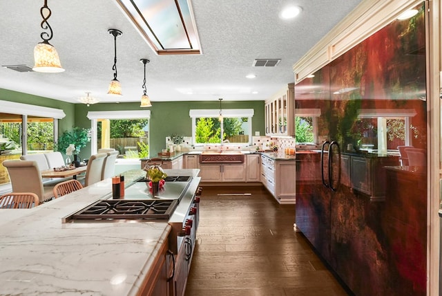 kitchen with visible vents, glass insert cabinets, decorative light fixtures, light stone counters, and dark wood-style floors