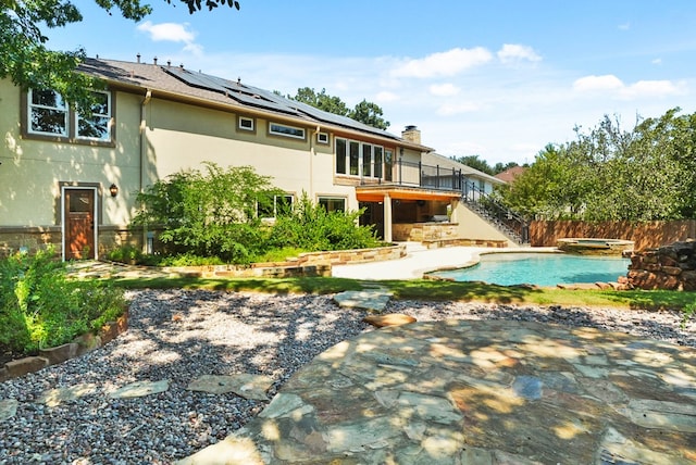 back of property featuring stucco siding, an in ground hot tub, fence, solar panels, and a patio area