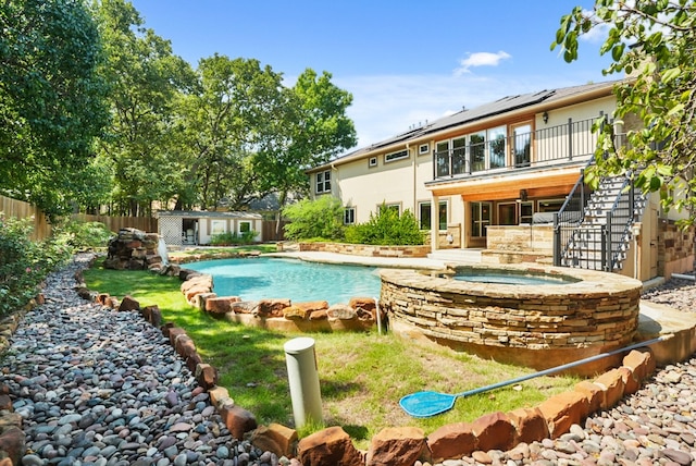 pool with an in ground hot tub, stairway, an outbuilding, and a fenced backyard