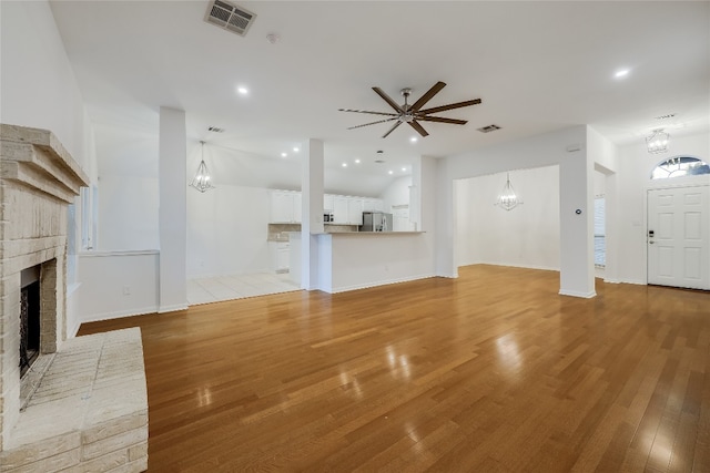 unfurnished living room with ceiling fan with notable chandelier, light hardwood / wood-style floors, and a fireplace