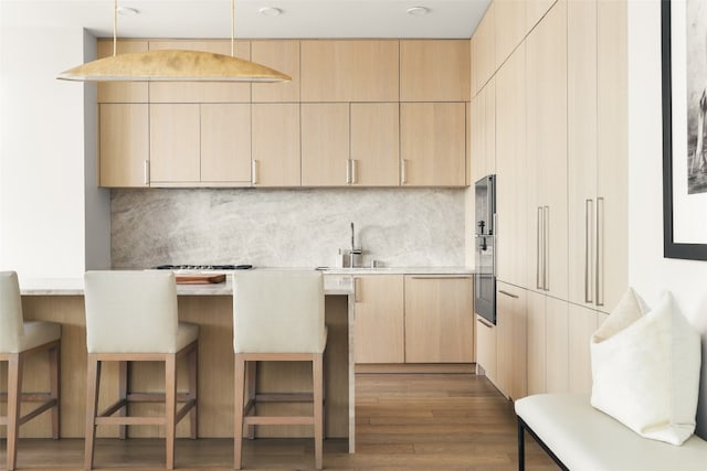 kitchen featuring a breakfast bar area, decorative light fixtures, light brown cabinetry, and dark hardwood / wood-style flooring