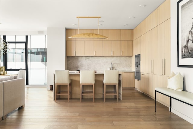 kitchen with light hardwood / wood-style flooring, light brown cabinets, hanging light fixtures, and a kitchen bar