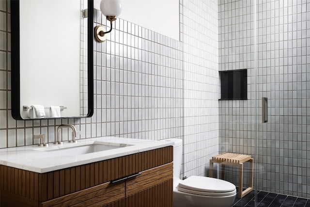 bathroom featuring toilet, a shower with shower door, vanity, and tile walls