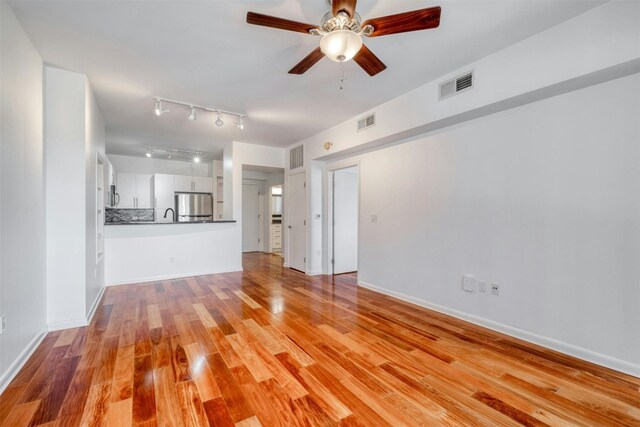 54 Rainey St Unit 1015, Austin, TX 78701 - unfurnished living room featuring a ceiling fan, light wood finished floors, rail lighting, and baseboards