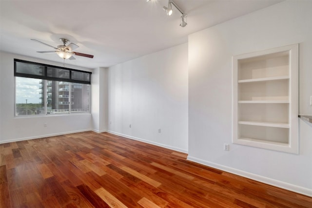 empty room featuring wood-type flooring, ceiling fan, and built in shelves