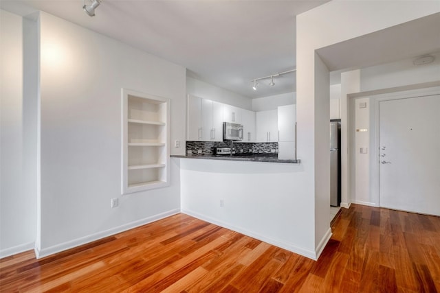 kitchen with tasteful backsplash, wood-type flooring, track lighting, white cabinetry, and stainless steel appliances