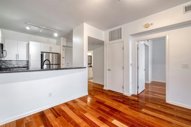 kitchen featuring light wood-type flooring, stainless steel refrigerator, white cabinetry, and dark stone counters