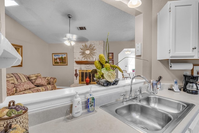 kitchen with white cabinets, a stone fireplace, a textured ceiling, ceiling fan, and sink