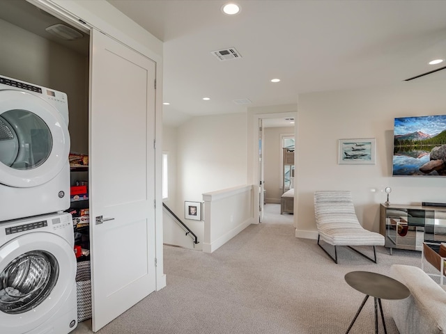 laundry area featuring stacked washer / drying machine and light carpet