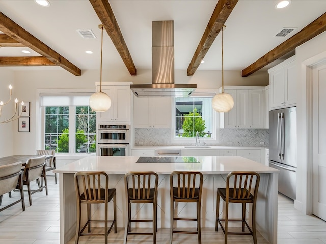 kitchen with appliances with stainless steel finishes, white cabinetry, island exhaust hood, beam ceiling, and a large island