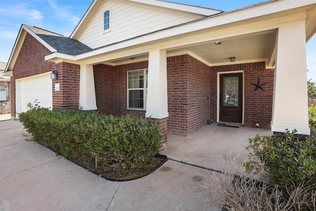 doorway to property with brick siding, a porch, and a garage