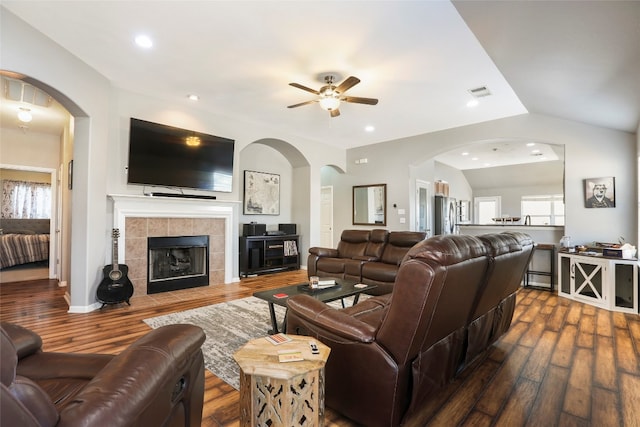 living room with lofted ceiling, dark hardwood / wood-style floors, a tile fireplace, and ceiling fan