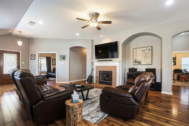 living area with a ceiling fan, dark wood finished floors, a tiled fireplace, arched walkways, and recessed lighting