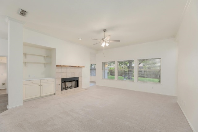 unfurnished living room featuring ornamental molding, a tiled fireplace, ceiling fan, and light colored carpet