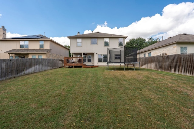 rear view of house featuring a trampoline, a wooden deck, and a yard