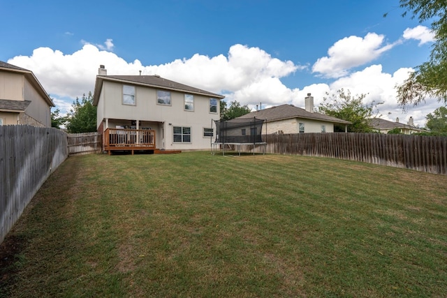 rear view of house featuring a yard, a deck, and a trampoline