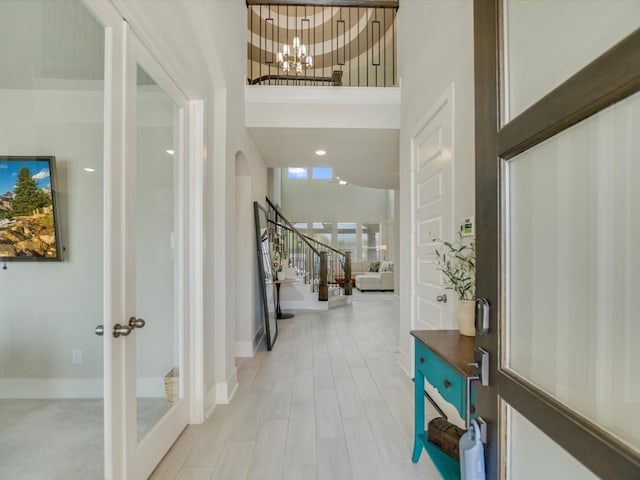 entryway featuring a chandelier, french doors, a towering ceiling, and light wood-type flooring