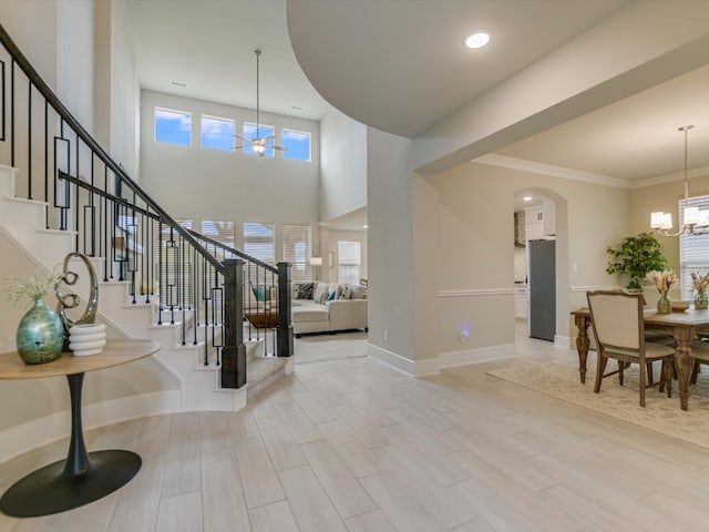 foyer featuring a towering ceiling, light hardwood / wood-style floors, crown molding, and a notable chandelier