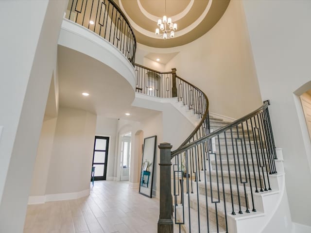 staircase with a chandelier, a towering ceiling, and hardwood / wood-style flooring