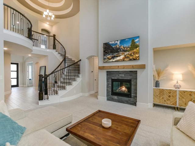 carpeted living room with a chandelier, a high ceiling, and a stone fireplace