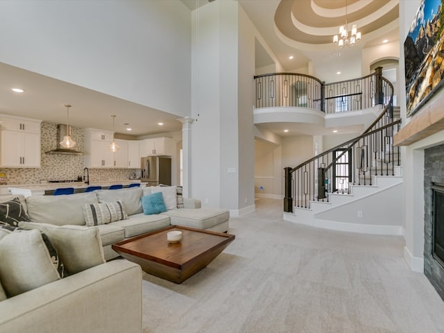 living room with a tile fireplace, a high ceiling, light colored carpet, and a notable chandelier