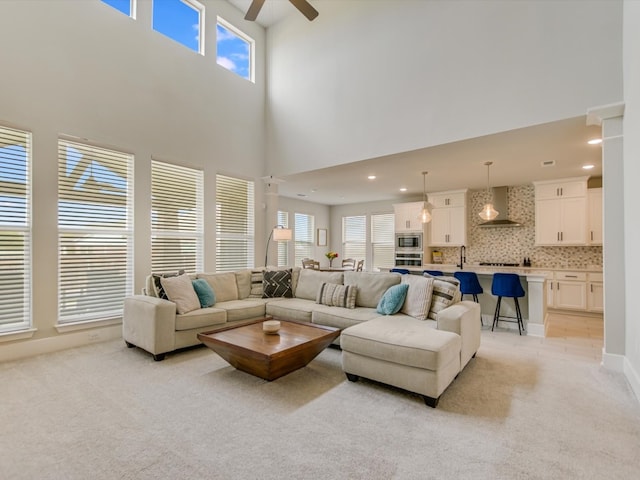 carpeted living room featuring ceiling fan, sink, and a high ceiling