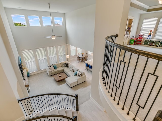 stairway with ceiling fan, hardwood / wood-style floors, a healthy amount of sunlight, and a high ceiling