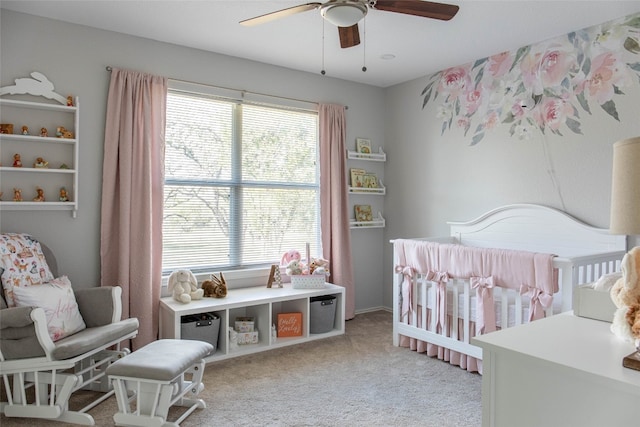 carpeted bedroom featuring ceiling fan and a nursery area