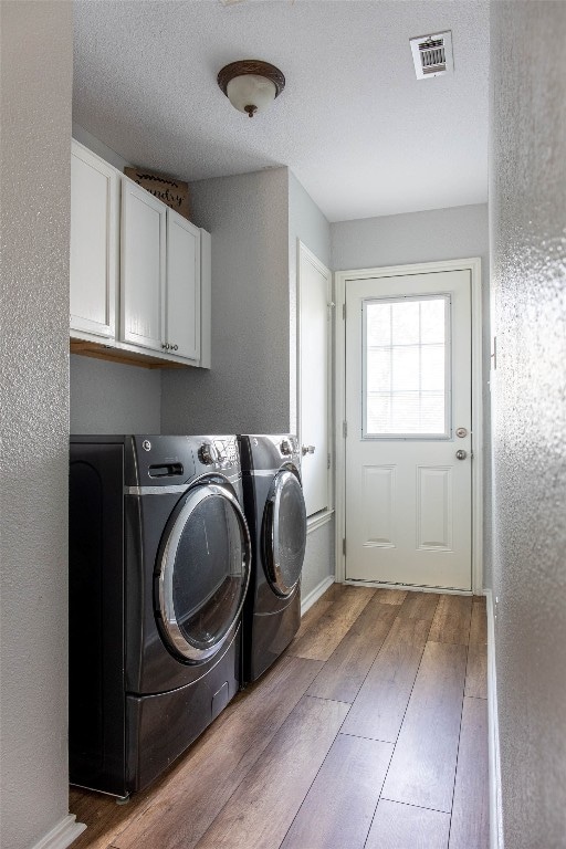 clothes washing area featuring cabinets, a textured ceiling, dark hardwood / wood-style floors, and washer and clothes dryer