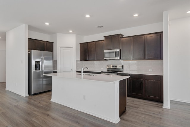 kitchen with sink, an island with sink, light hardwood / wood-style flooring, stainless steel appliances, and backsplash