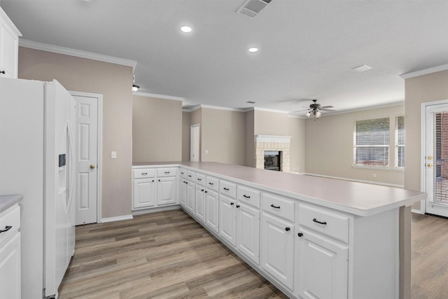 kitchen featuring white refrigerator with ice dispenser, light wood-type flooring, a fireplace, white cabinetry, and kitchen peninsula