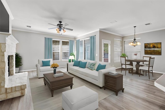 living room with a stone fireplace, crown molding, light hardwood / wood-style floors, and ceiling fan with notable chandelier