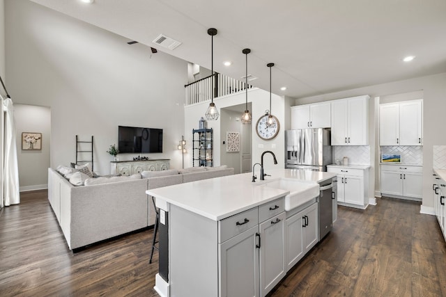 kitchen featuring appliances with stainless steel finishes, backsplash, a center island with sink, and white cabinetry