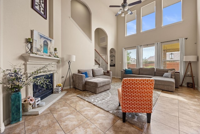 tiled living room with a fireplace, ceiling fan, and a high ceiling