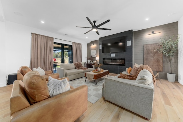 living room with ceiling fan, a fireplace, light wood-type flooring, and wood walls