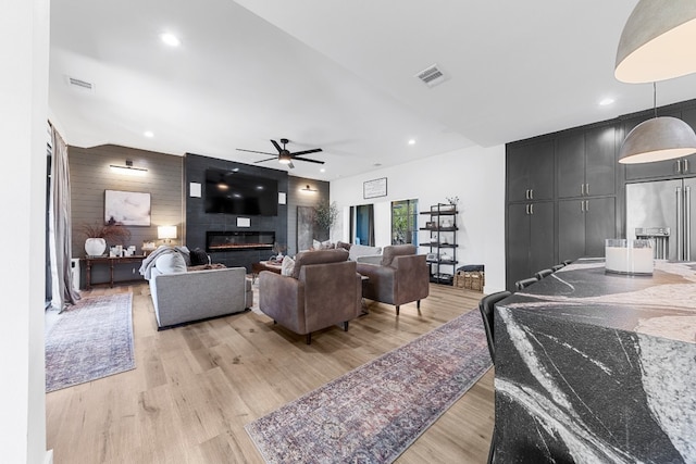 living room featuring ceiling fan, a fireplace, light wood-type flooring, and wood walls